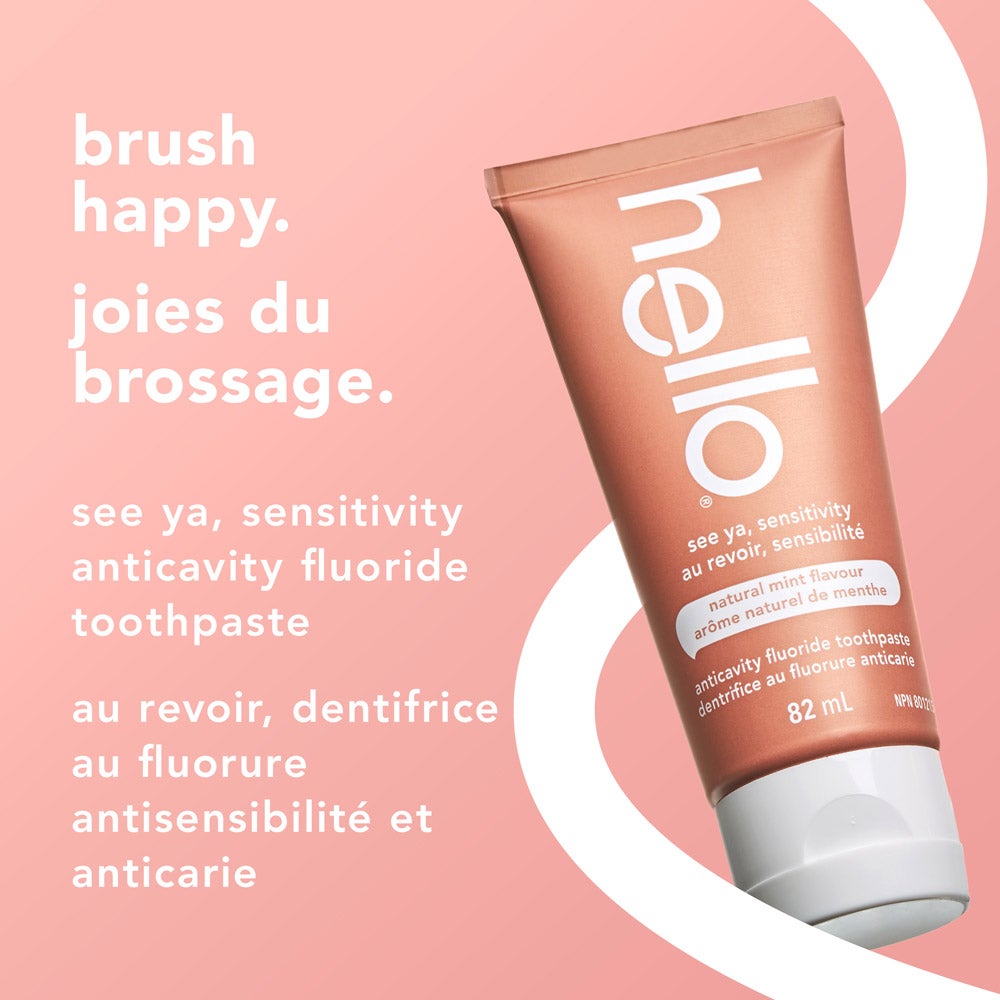 A tube of hello See Ya Sensitivity toothpaste, natural mint flavor, displayed at an angle on a light pink and white curved background. Text above and beside the tube reads "brush happy" and "see ya, sensitivity anticavity fluoride toothpaste" in both English and French.