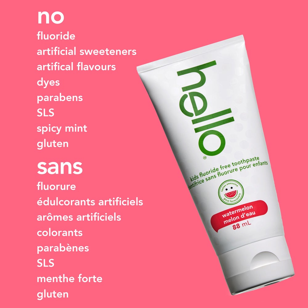 A tube of hello kids watermelon fluoride free toothpaste is angled on a solid pink background. The text beside it lists what the product does not contain: "no fluoride, artificial sweeteners, artificial flavours, dyes, parabens, SLS, spicy mint, gluten."
