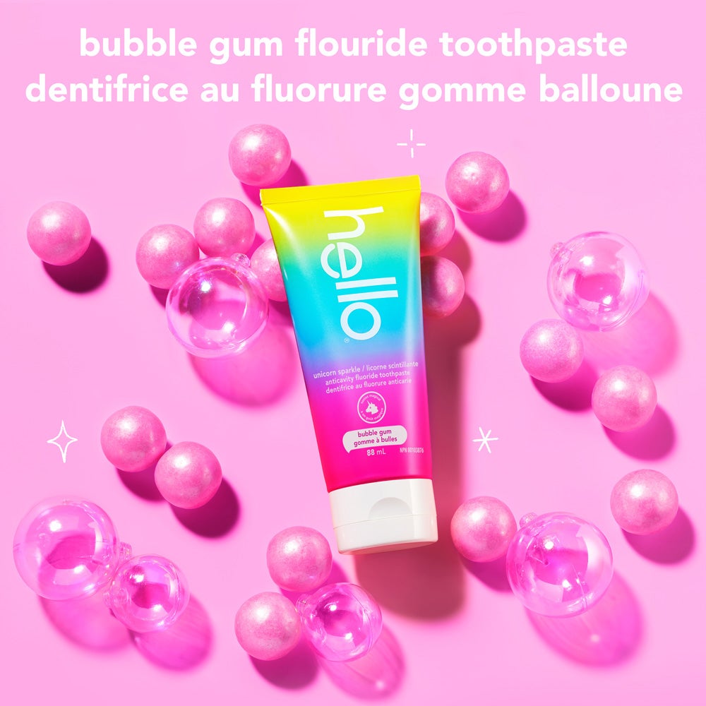 A tube of hello unicorn sparkle bubble gum fluoride toothpaste is placed among scattered pink bubble gum balls and clear bubbles on a light pink background. The text above reads, "bubble gum fluoride toothpaste."