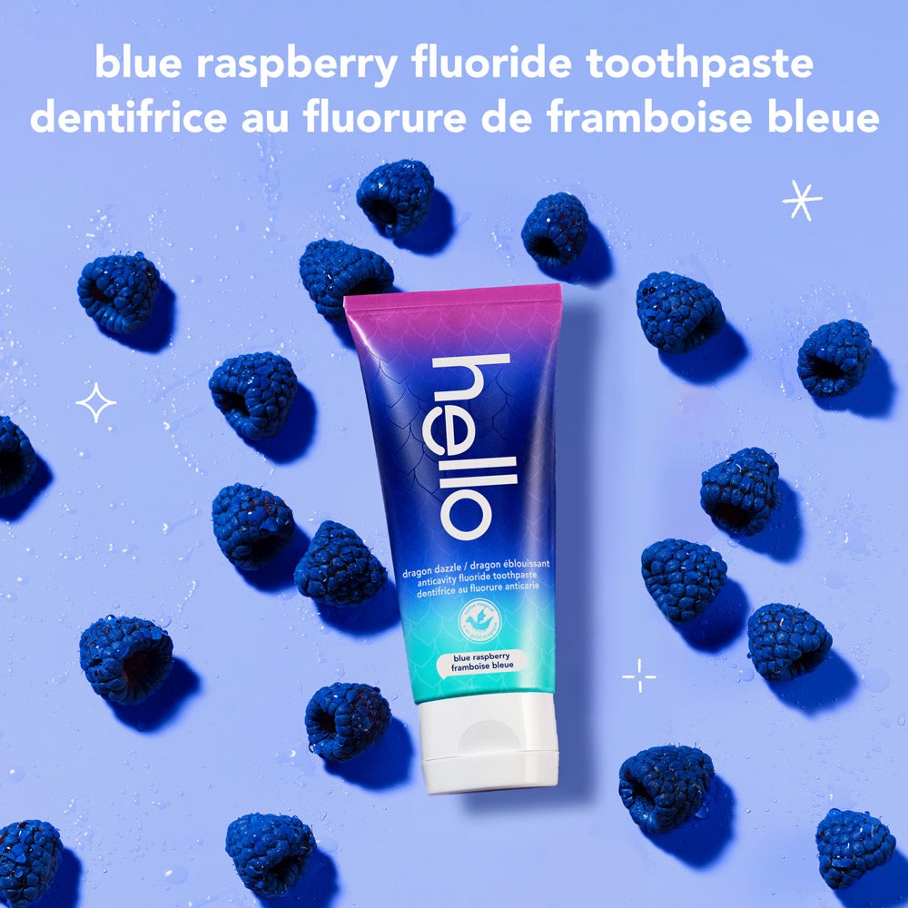 A tube of hello dragon dazzle blue raspberry fluoride toothpaste is surrounded by several fresh blue raspberries on a light blue background. The text reads, "blue raspberry fluoride toothpaste."